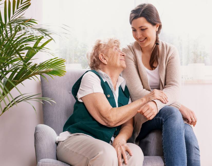 Personne senior et son auxiliaire de vie assises sur fauteuil, souriantes